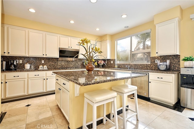 kitchen featuring a kitchen island, white cabinetry, appliances with stainless steel finishes, dark stone counters, and decorative backsplash