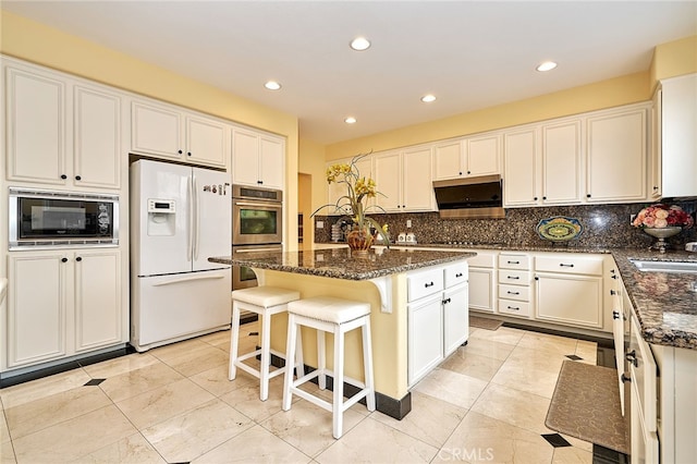 kitchen with dark stone counters, white refrigerator with ice dispenser, a kitchen island with sink, and tasteful backsplash