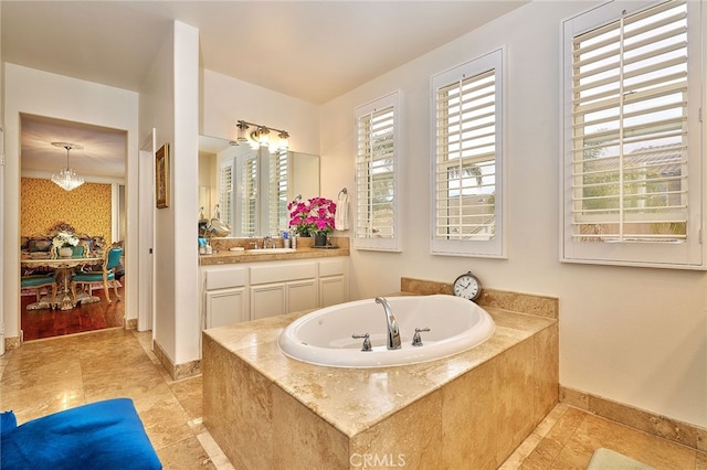 bathroom featuring a chandelier, tiled tub, and vanity