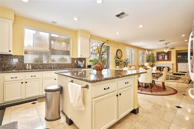 kitchen featuring dark stone counters, backsplash, a kitchen island, and ceiling fan