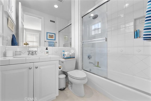 bathroom with toilet, bath / shower combo with glass door, visible vents, and vanity