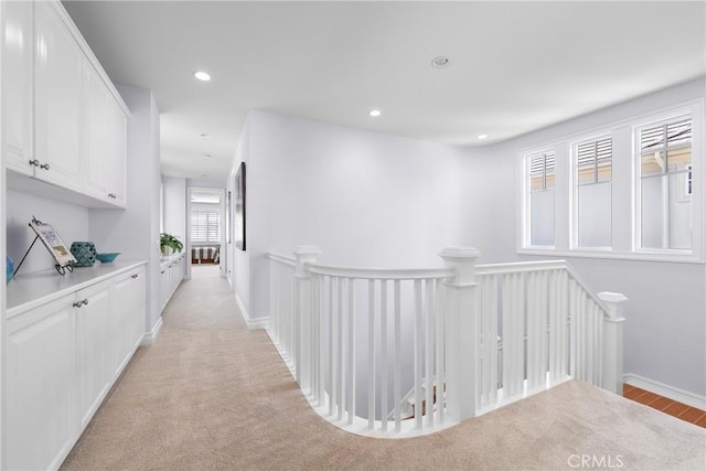 hallway featuring light colored carpet, recessed lighting, baseboards, and an upstairs landing