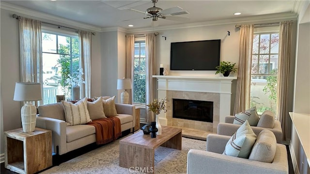 living area with a healthy amount of sunlight, ceiling fan, ornamental molding, and a tiled fireplace