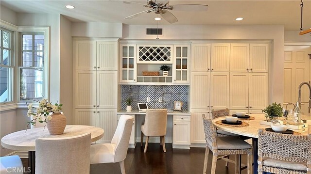 kitchen featuring dark hardwood / wood-style flooring, light stone counters, ceiling fan, and backsplash