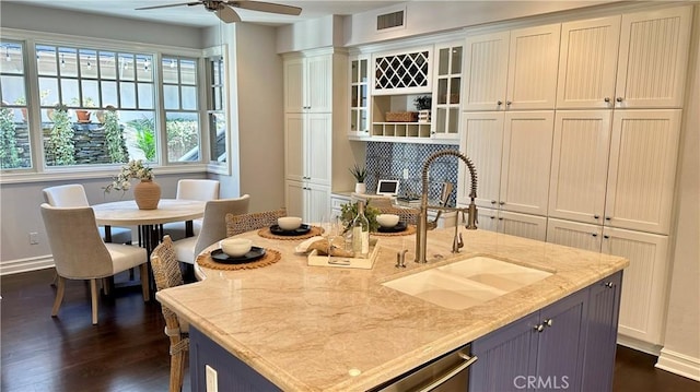 kitchen with light stone counters, dark wood-style flooring, visible vents, glass insert cabinets, and a sink