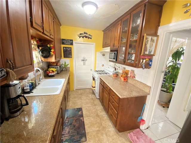 kitchen with light tile patterned floors, white gas range oven, sink, and backsplash