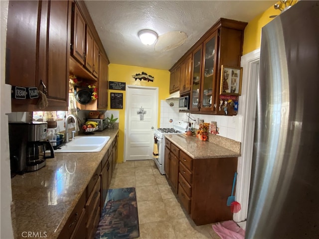 kitchen featuring white gas range, dark stone counters, sink, a textured ceiling, and tasteful backsplash