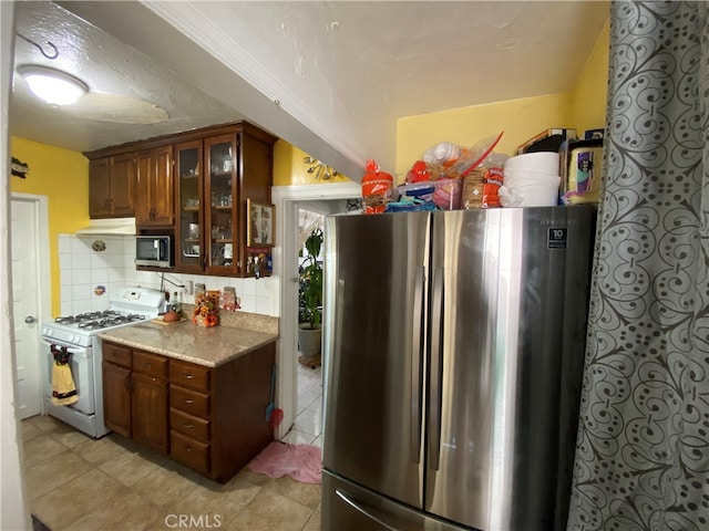 kitchen with stainless steel appliances, light stone countertops, light tile patterned floors, a textured ceiling, and tasteful backsplash