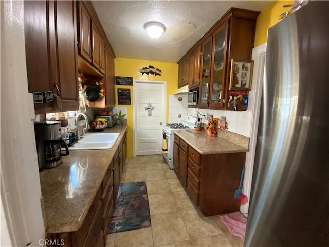 kitchen featuring tasteful backsplash, a textured ceiling, dark stone countertops, sink, and white gas range oven