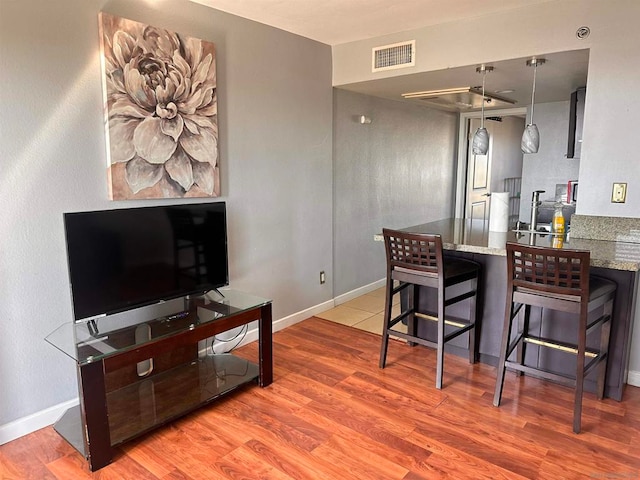 interior space featuring a kitchen breakfast bar, kitchen peninsula, light stone countertops, light wood-type flooring, and decorative light fixtures