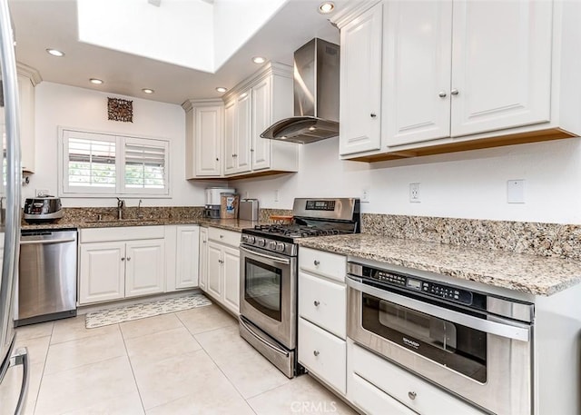 kitchen with light stone countertops, stainless steel appliances, sink, wall chimney range hood, and white cabinets