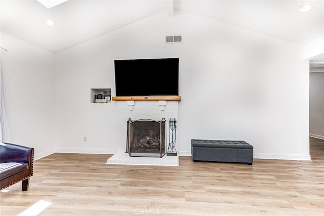 living room featuring light wood-type flooring, lofted ceiling with beams, and a fireplace