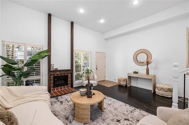 living room with dark wood-type flooring, high vaulted ceiling, and a brick fireplace