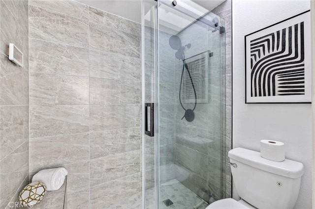 bathroom featuring a shower with door and toilet