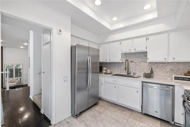 kitchen with sink, white cabinets, backsplash, a tray ceiling, and stainless steel appliances