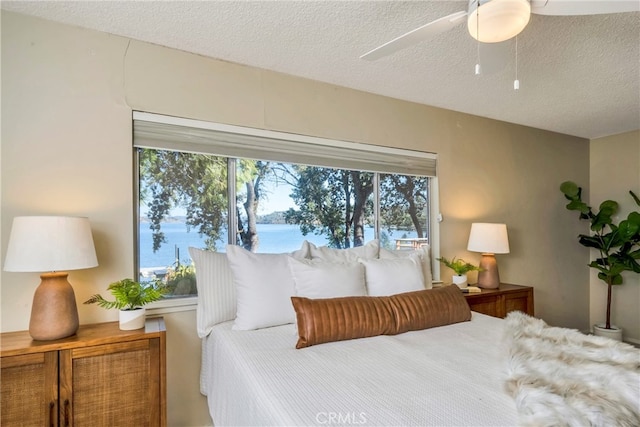 bedroom with a water view, a textured ceiling, multiple windows, and ceiling fan