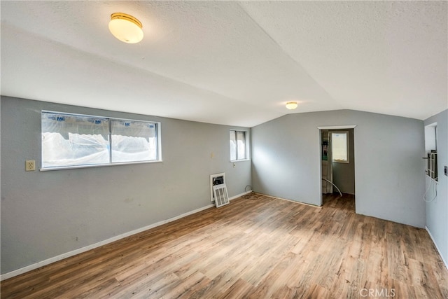 interior space featuring vaulted ceiling, a textured ceiling, heating unit, and hardwood / wood-style floors