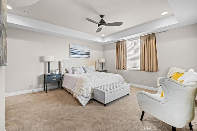 bedroom with light colored carpet, ceiling fan, and a tray ceiling