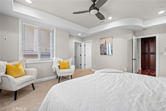 bedroom with a raised ceiling, light colored carpet, and ceiling fan