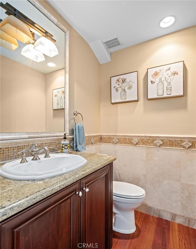 bathroom with wood-type flooring, tile walls, vanity, and toilet