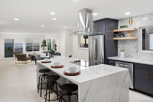 kitchen featuring island exhaust hood, appliances with stainless steel finishes, light stone countertops, a kitchen island, and a breakfast bar