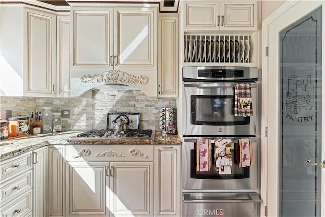 kitchen featuring appliances with stainless steel finishes, cream cabinets, stone counters, and decorative backsplash