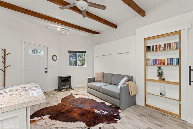 living room featuring beam ceiling, light hardwood / wood-style flooring, ceiling fan, and a wood stove