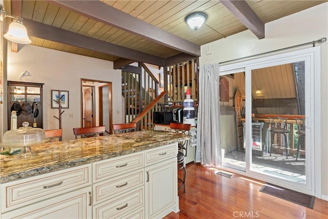 kitchen with cream cabinets, beamed ceiling, hanging light fixtures, light stone countertops, and light hardwood / wood-style flooring