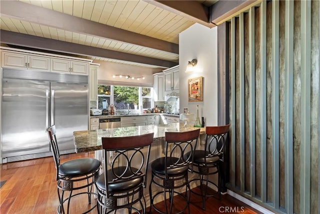 kitchen featuring appliances with stainless steel finishes, stone countertops, beamed ceiling, backsplash, and light wood-type flooring