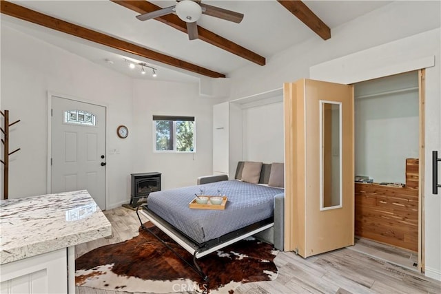 bedroom with beam ceiling, a wood stove, ceiling fan, and light hardwood / wood-style flooring