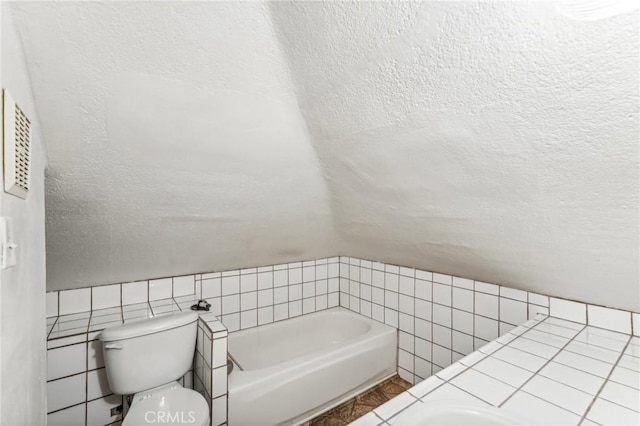 bathroom with a tub to relax in, a textured ceiling, tile walls, toilet, and lofted ceiling