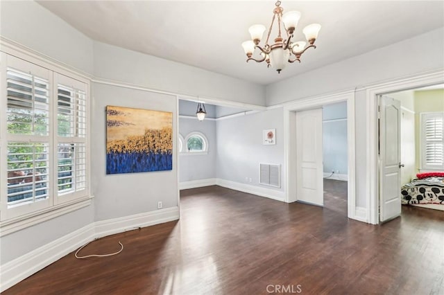 spare room with dark hardwood / wood-style flooring, an inviting chandelier, and plenty of natural light