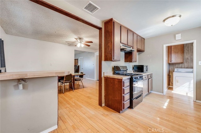 kitchen with ceiling fan, light wood-type flooring, a textured ceiling, gas stove, and washer / dryer