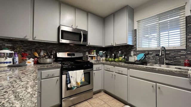 kitchen with light stone countertops, appliances with stainless steel finishes, tasteful backsplash, sink, and light tile patterned flooring