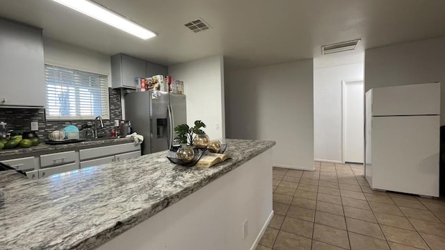 kitchen with white fridge, sink, stainless steel fridge with ice dispenser, light stone counters, and light tile patterned floors