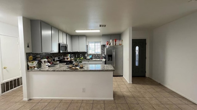 kitchen with light stone countertops, appliances with stainless steel finishes, decorative backsplash, sink, and light tile patterned flooring