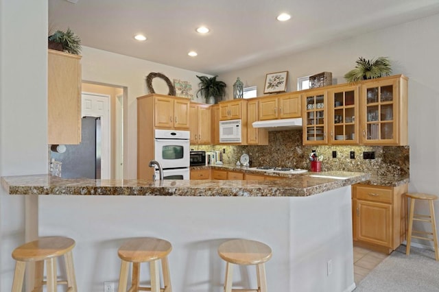 kitchen featuring a kitchen bar, white appliances, kitchen peninsula, and dark stone counters