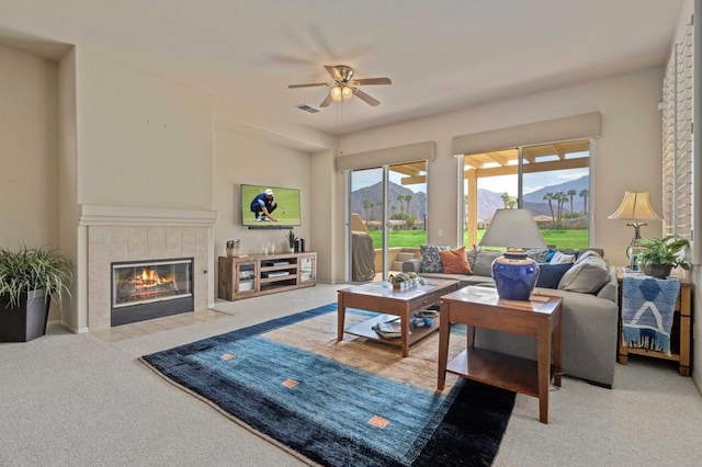 living room featuring a tiled fireplace, ceiling fan, and light carpet