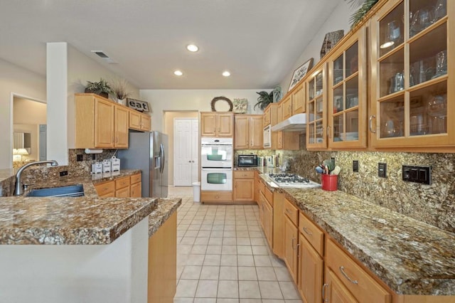 kitchen with stone counters, sink, kitchen peninsula, white appliances, and decorative backsplash