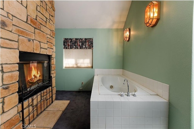 bathroom with a relaxing tiled tub, a stone fireplace, and lofted ceiling