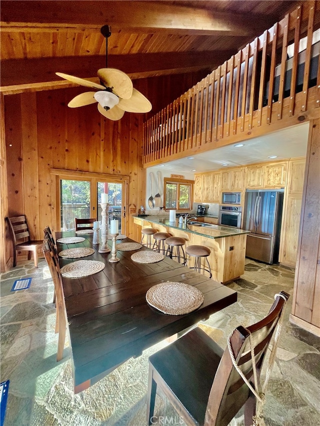 dining area with high vaulted ceiling, ceiling fan, wooden walls, sink, and beam ceiling