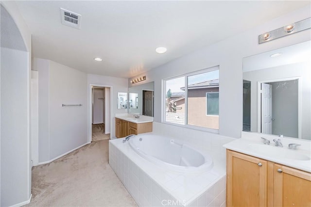 bathroom featuring a relaxing tiled tub and vanity