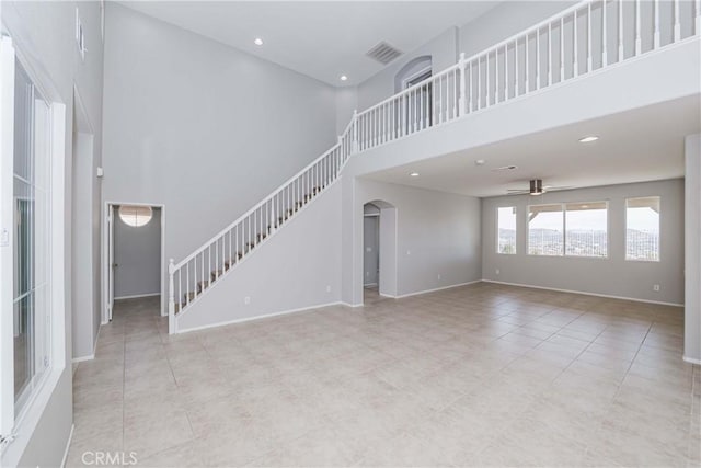 unfurnished living room with ceiling fan, light tile patterned floors, and a high ceiling