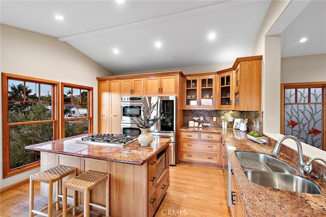 kitchen with sink, lofted ceiling, light stone countertops, appliances with stainless steel finishes, and a center island