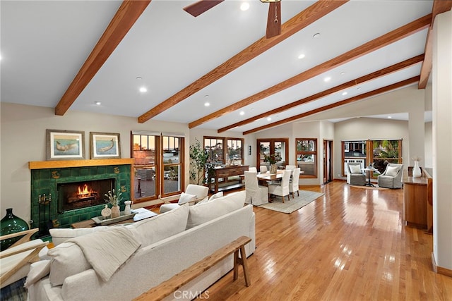 living room featuring lofted ceiling with beams, a tiled fireplace, and light wood-type flooring