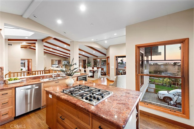 kitchen with vaulted ceiling with skylight, light hardwood / wood-style flooring, light stone counters, stainless steel appliances, and a center island