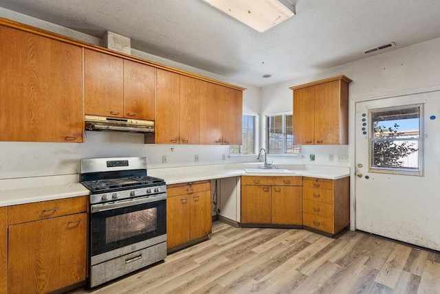 kitchen with light wood-type flooring, a textured ceiling, stainless steel gas stove, and sink