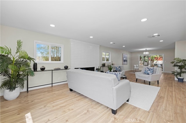 living room with light wood-type flooring, a notable chandelier, and a brick fireplace