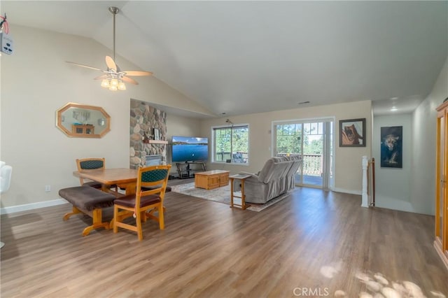 living room with ceiling fan, a stone fireplace, wood-type flooring, and vaulted ceiling