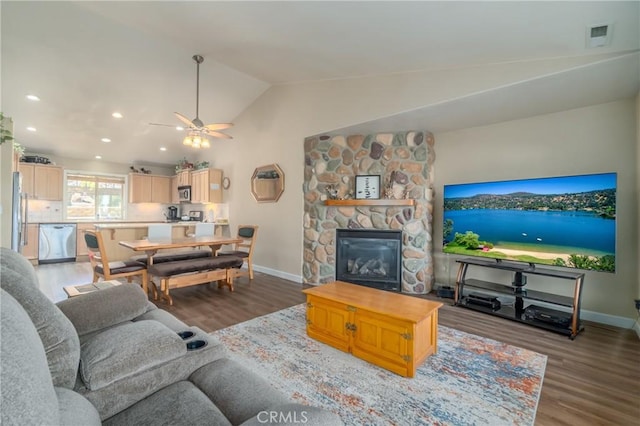 living room featuring dark hardwood / wood-style floors, vaulted ceiling, ceiling fan, and a stone fireplace